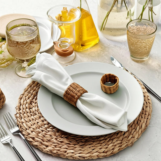 A set of handwoven water hyacinth napkin rings displayed on a table setting, with a white napkin and cutlery in the background.