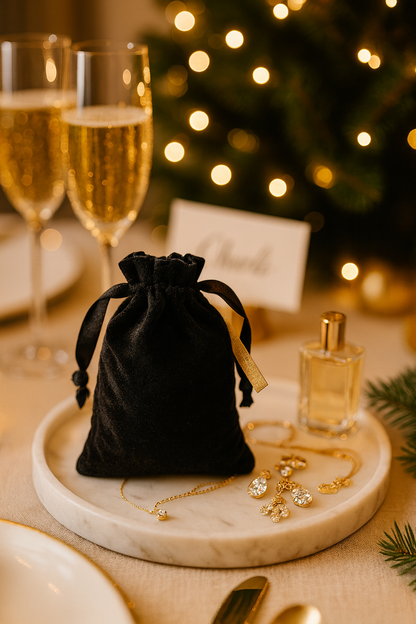 Black velvet drawstring bag wedding favor with jewelry on a marble tray in front of a Christmas tree.